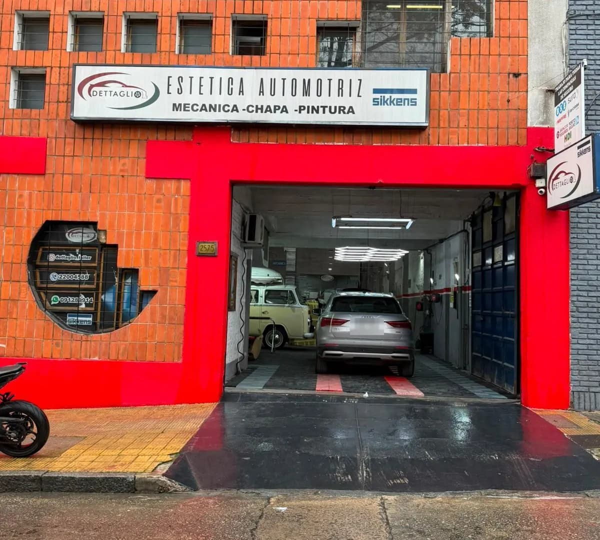 Frente de la sucursal de Goes del taller Dettaglio: fachada de ladrillo con el portón enmarcado en rojo y autos dentro del taller
