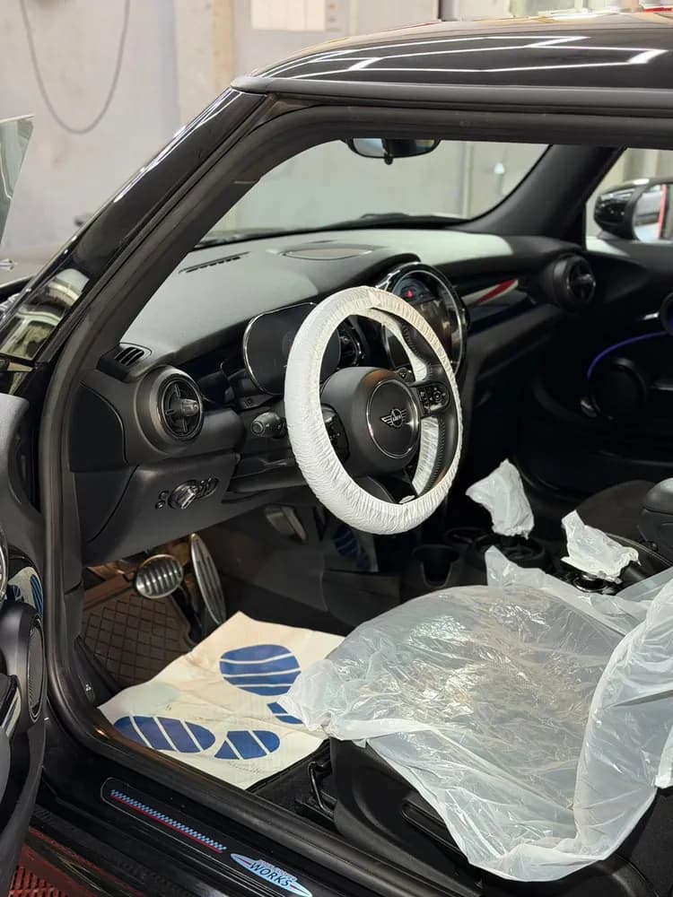 Interior de un auto en proceso, con el volante enfundado y el asiento cubierto con protecciones plásticas