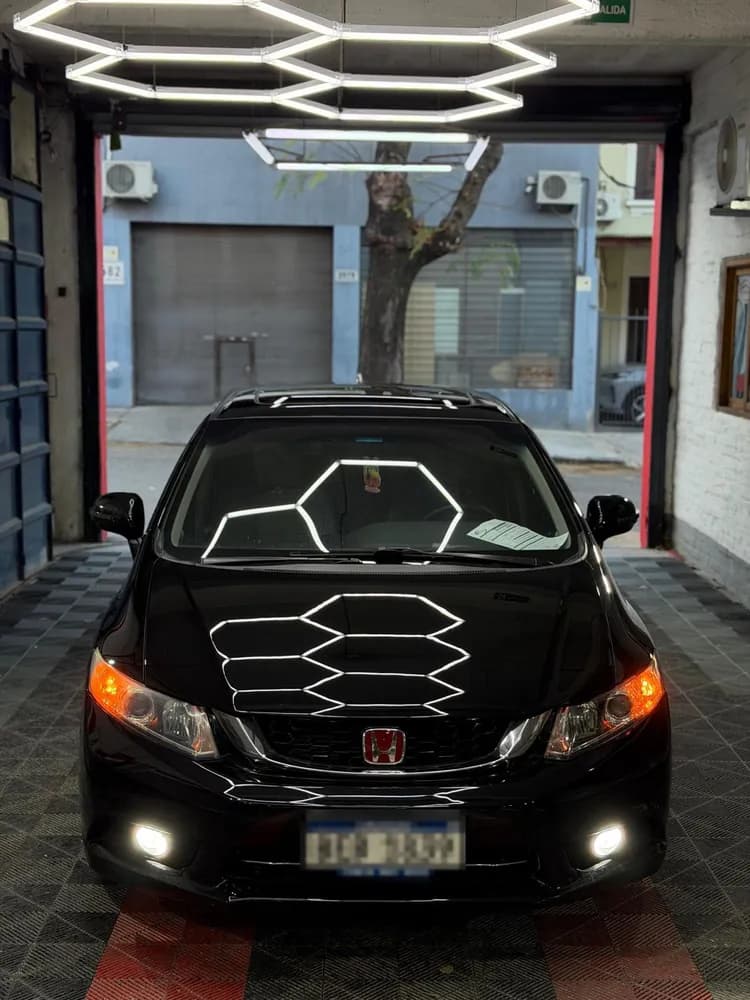 Auto negro de frente en la puerta del taller, con el reflejo de la lámpara hexagonal sobre el capó